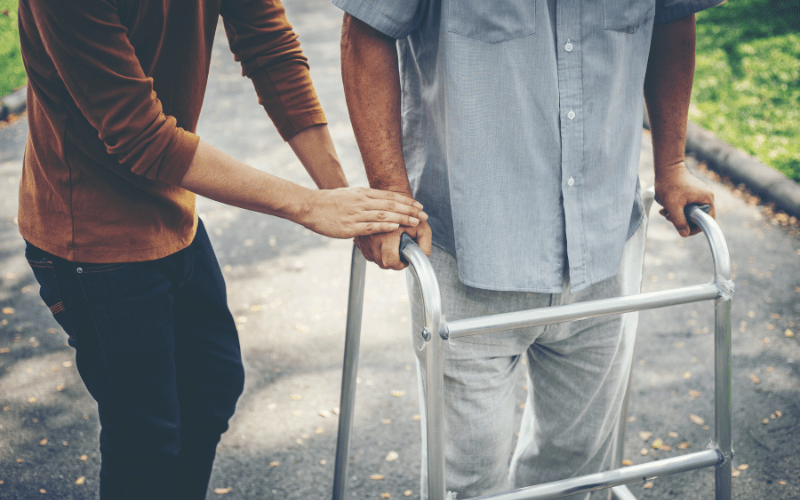 adult son helping elderly father use his walker outside