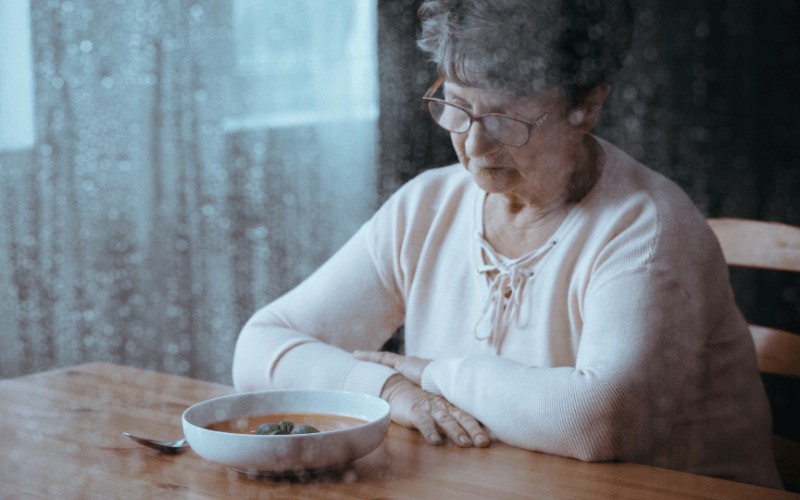 elderly woman staring at a bowl of soup