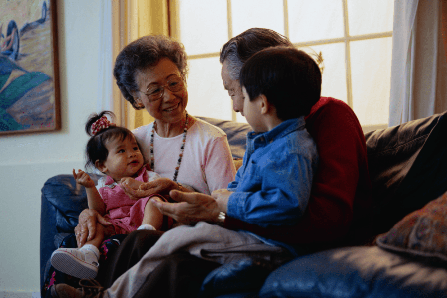 Summer activities for seniors - Grandparents happily talking to their two grandchildren on the couch - MeetCaregivers