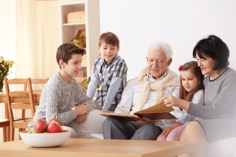 Summer activities for seniors - Grandparents looking at a photo album with their grandchildren - MeetCaregivers