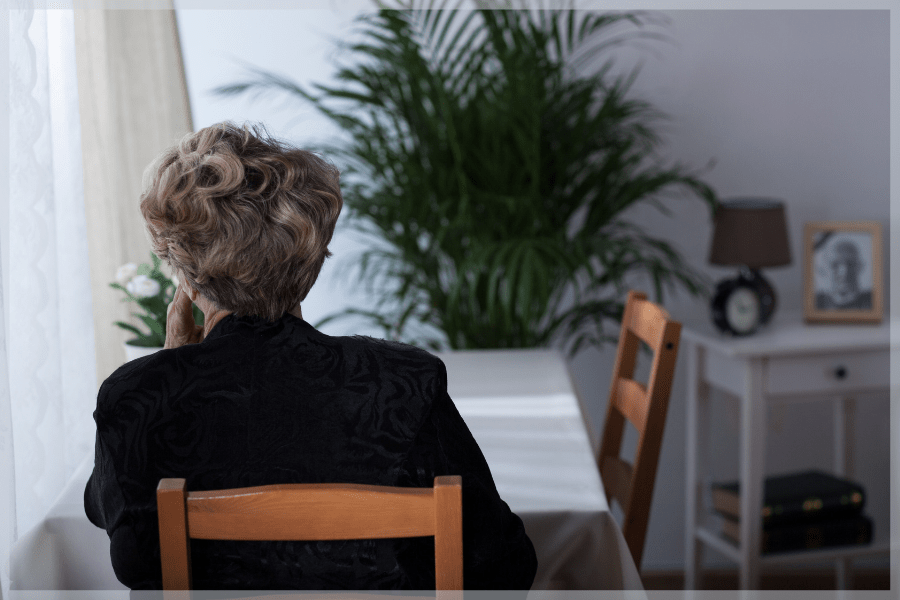 Depression in the elderly - Senior woman sitting alone at her kitchen table looking out the window - MeetCaregivers