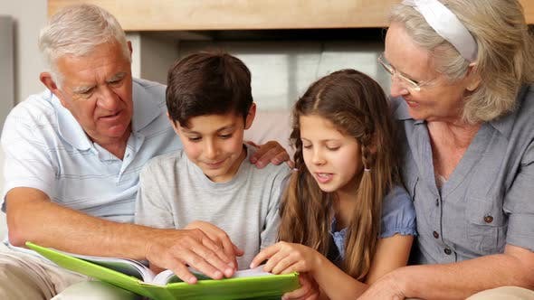 Summer Activities To Do With The Grandkids - Grandparents Looking At A Book With Grandchildren
