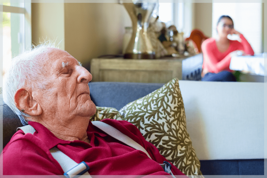 Poor sleep quality Elderly man sleeping in a chair while his caregiver watches him in the background MeetCaregivers