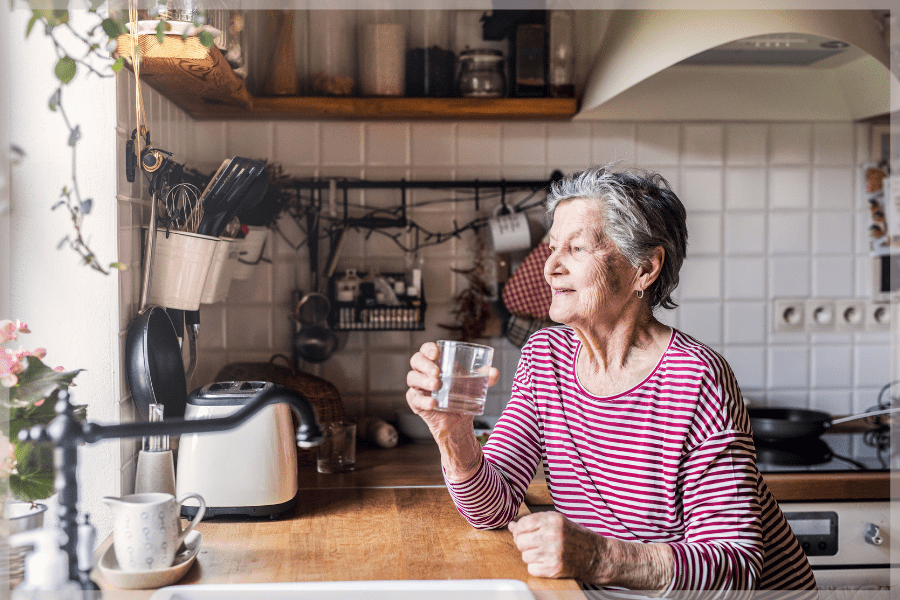 Summer safety tips Elderly woman standing in her kitchen drinking water MeetCaregivers