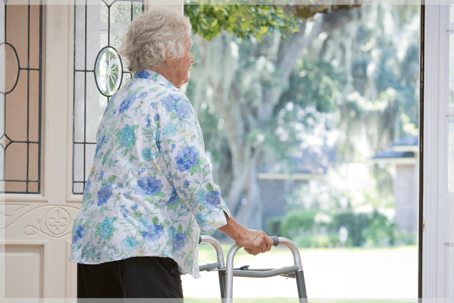 Summer safety tips - Elderly woman standing in the front door looking outside while holding her walker - MeetCaregivers