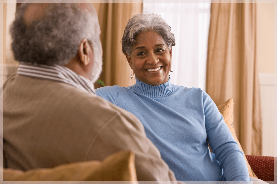 Safe at home - Middle aged woman talking to older man on the couch - MeetCaregivers