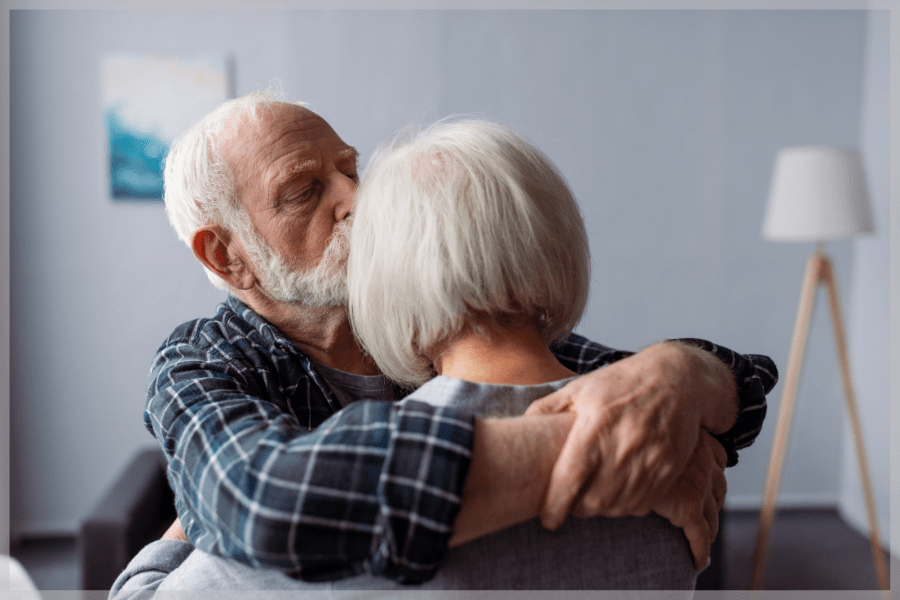 Alzheimer's Awareness Month - Elderly man holding his wife and giving her a kiss on the forehead - MeetCaregivers