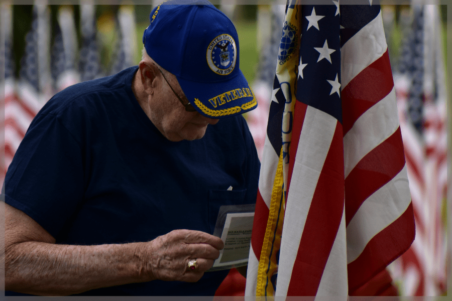Elderly veterans - Senior man standing in front of US flag reading notecard - MeetCaregivers