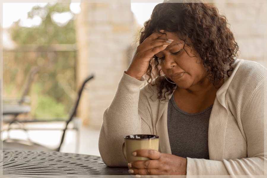National Family Caregivers Month - Stressed woman holding her head and a cup of coffee at an outdoor table - MeetCaregivers