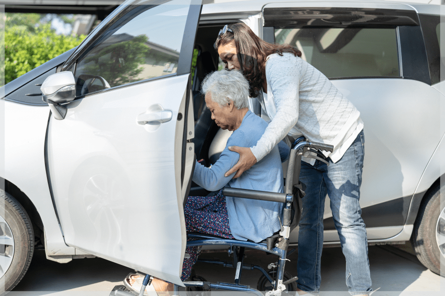 Talking To Your Elderly Parents About When To Stop Driving – Caregiver helping elderly woman from her wheelchair to a vehicle - MeetCaregivers