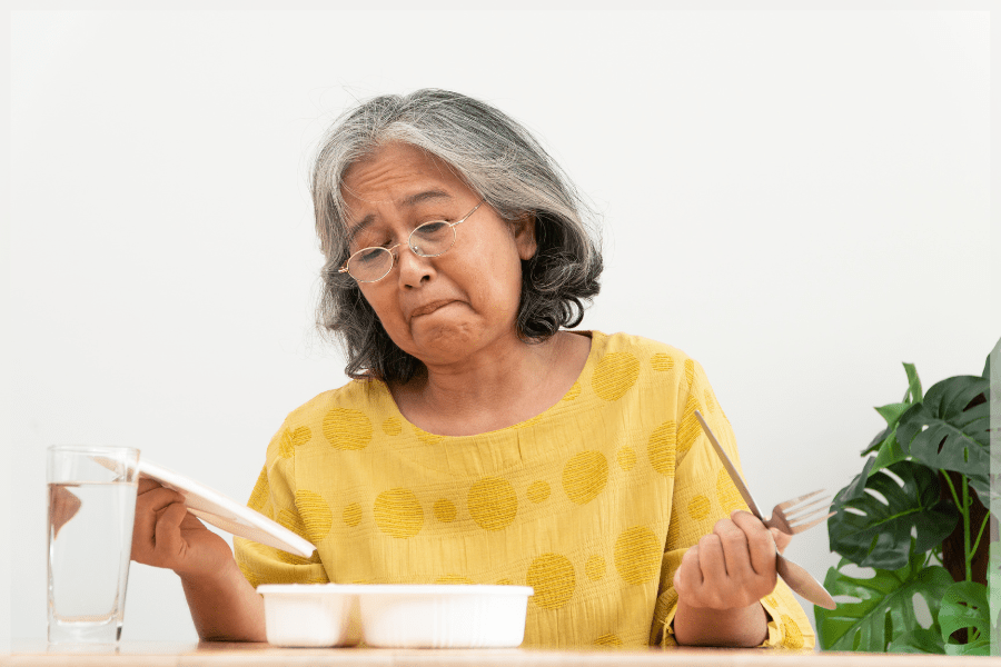 Appetite Loss In Elderly Adults - Senior woman looking unhappily at her meal - MeetCaregivers