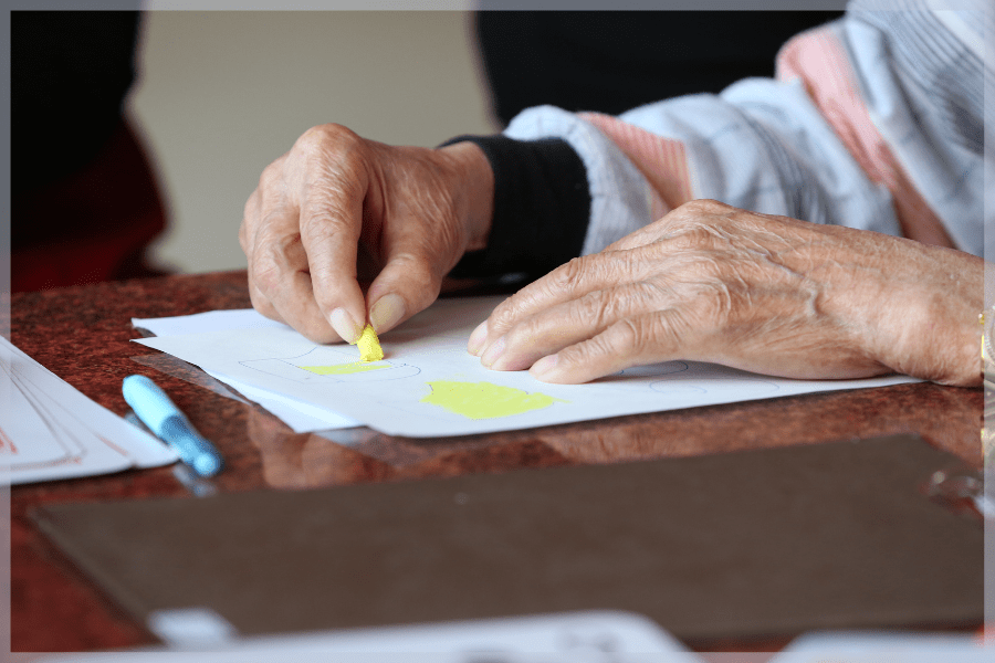 Activities for seniors with limited mobility - Elderly person coloring with a yellow crayon - MeetCaregivers