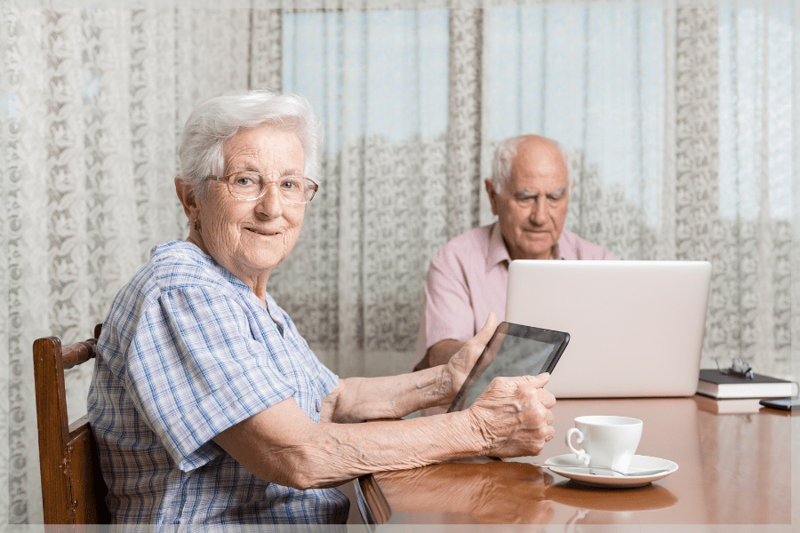 Activities for seniors with limited mobility - Happy senior couple reading on a tablet and laptop at the table - MeetCaregivers