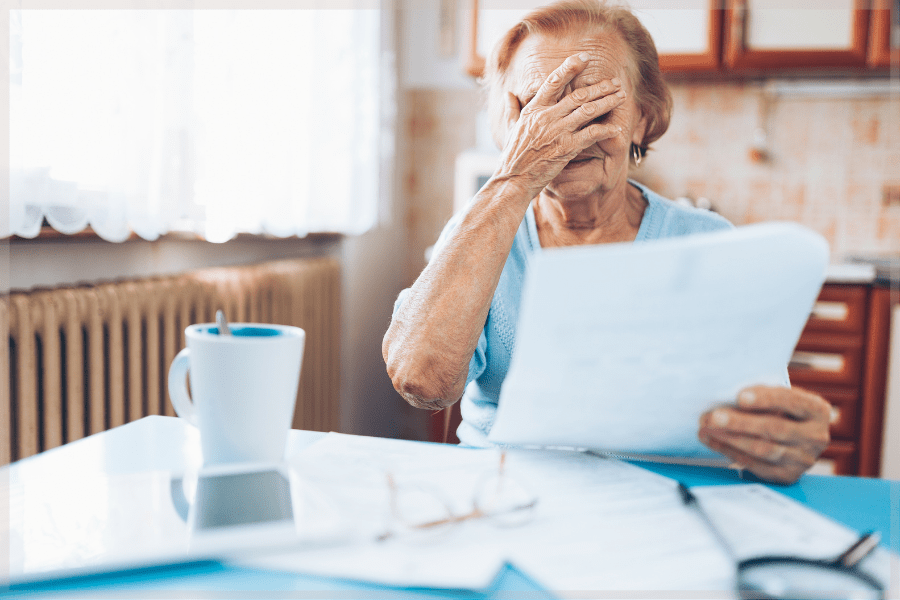 Stress Awareness Month - Stressed elderly woman reading paperwork at her kitchen table - MeetCaregivers