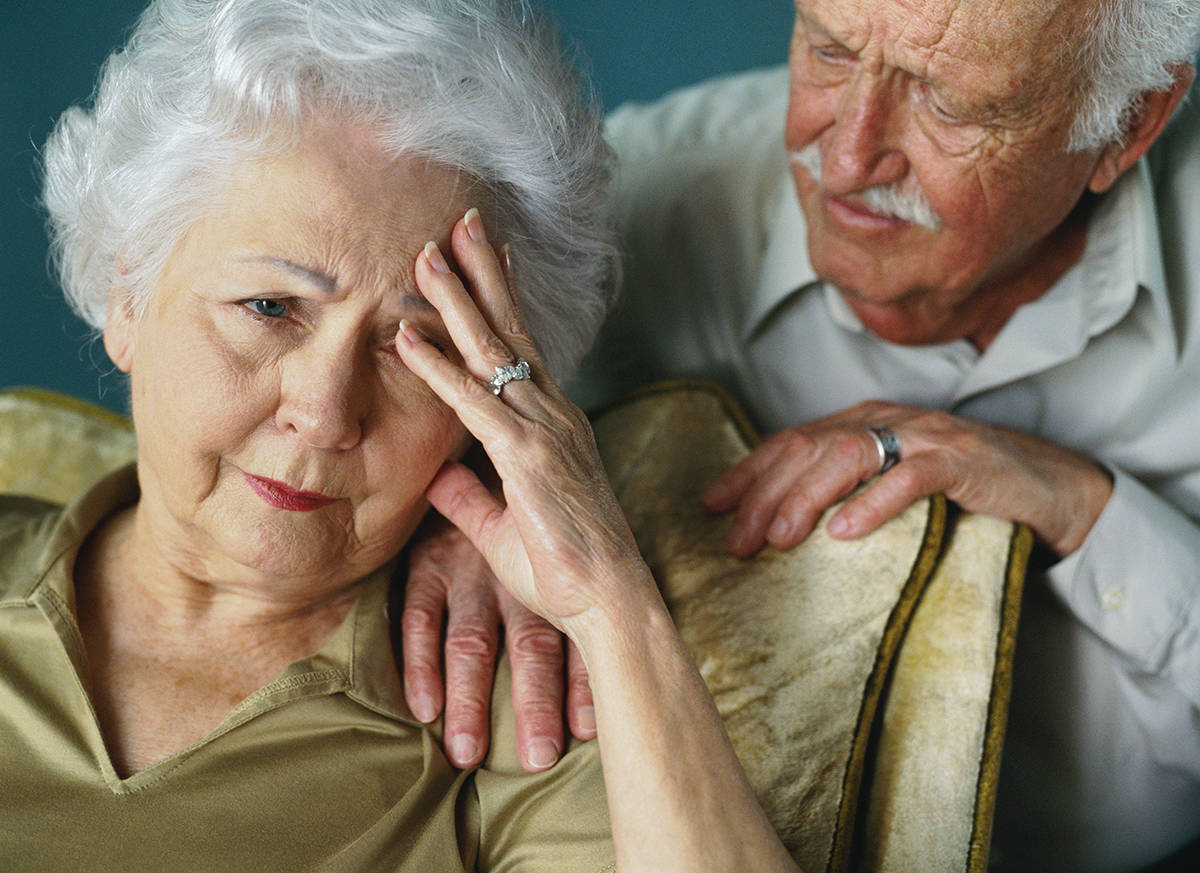 mental-health-month-an-elderly-woman-resting-her-head-in-her-hand-with-her-worried-husband-standing-behind-her