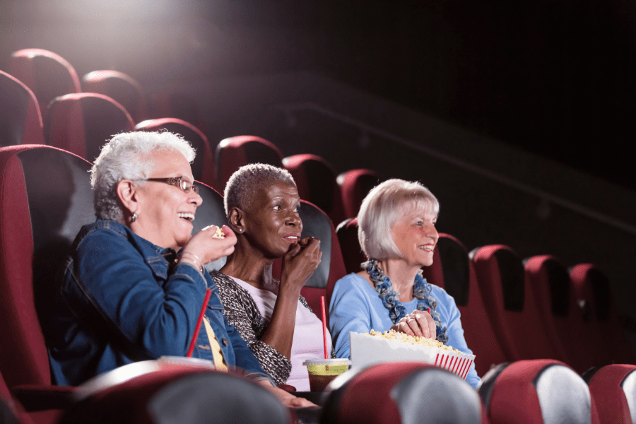 Group Of Senior Women Eating Popcorn And Watching A Movie At The Theatre