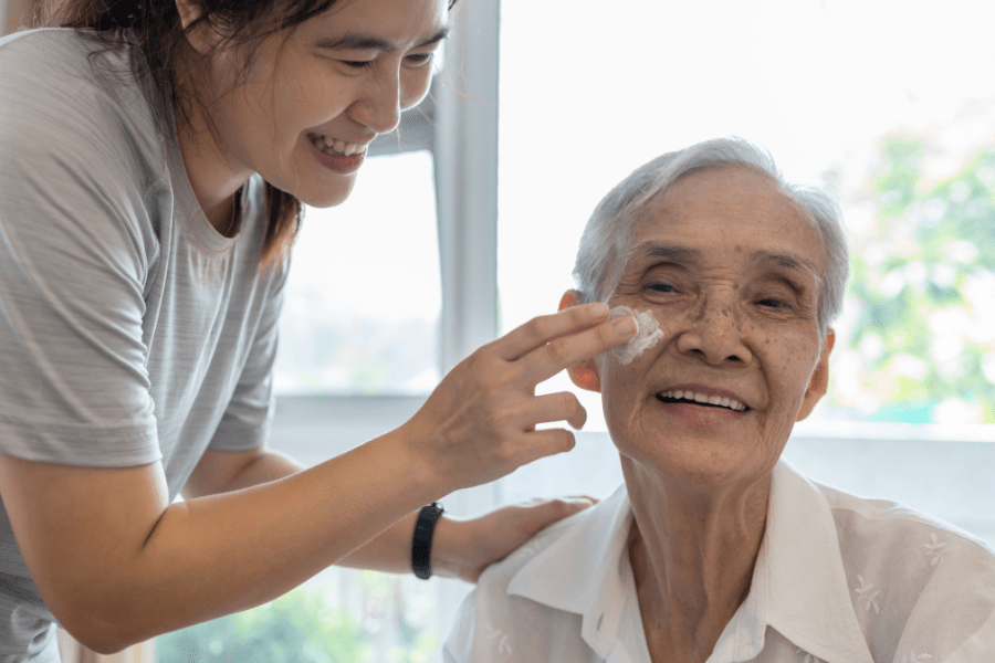 Skin Care For Seniors Caregiver Applying Sunscreen To Elderly Womans Cheeks
