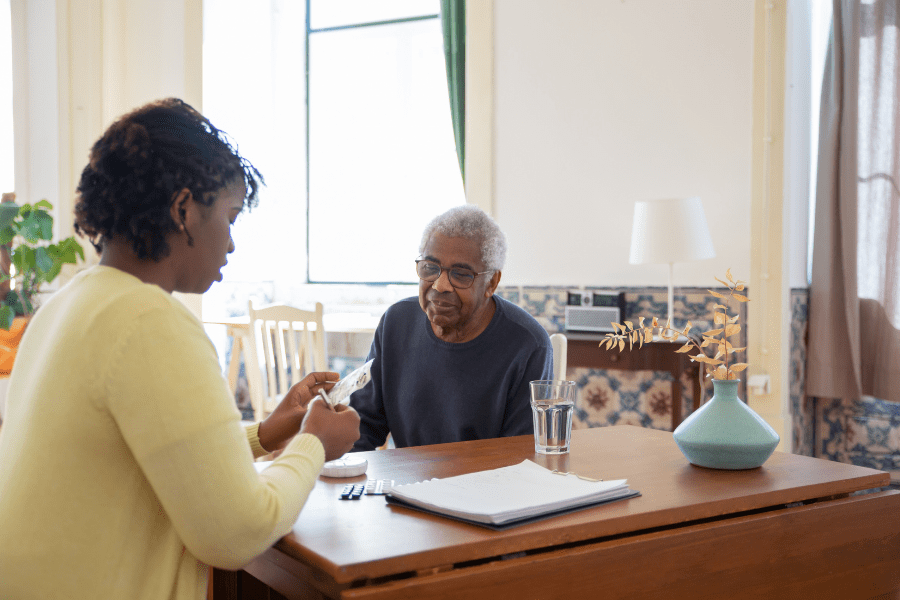 A woman in a yellow cardigan preparing medicine for an elderly man with swallowing problems.