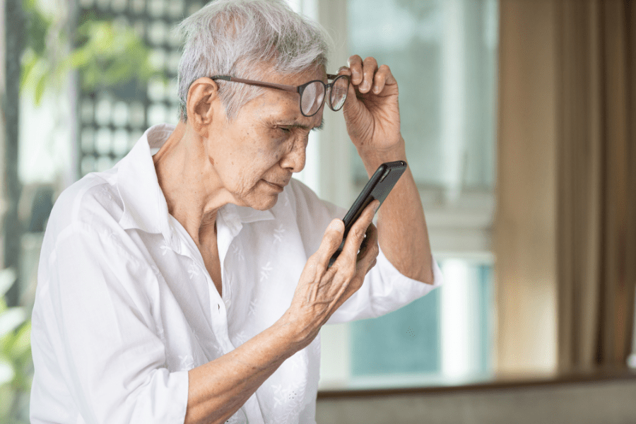 Senior woman without daily living aids lifting her glasses struggling to read smartphone