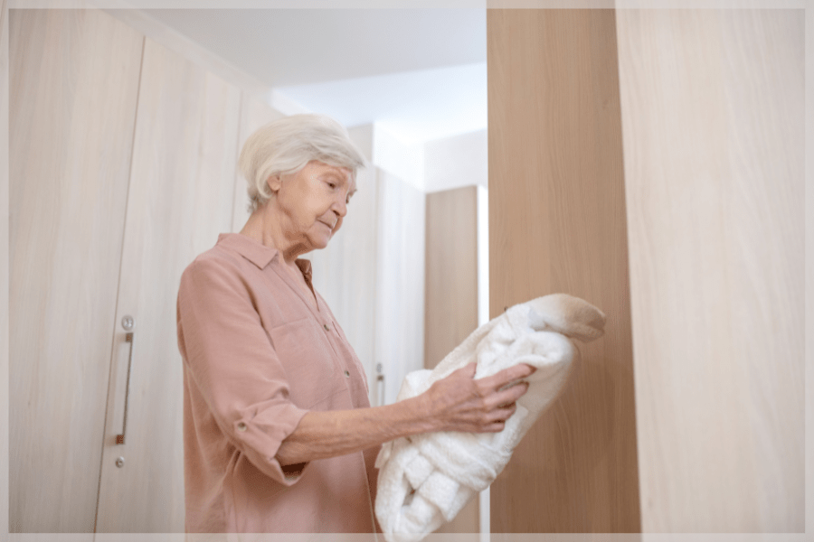 Downsizing for seniors - Elderly woman deciding to keep a folded bathrobe - MeetCaregivers