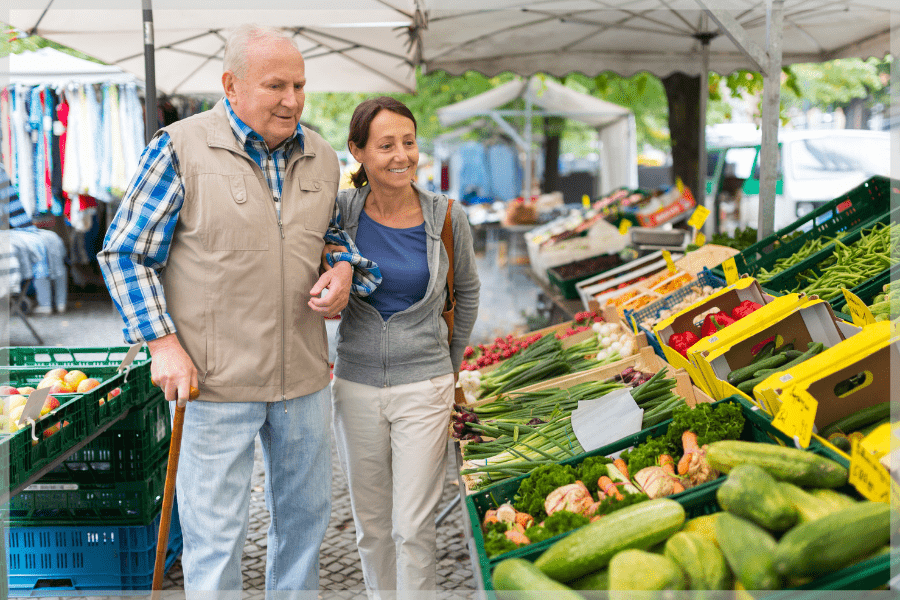 Paid caregiver - Adult daughter helping elderly father walk around open air market - MeetCaregivers