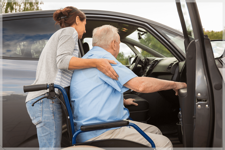 Resources for family caregivers - Woman ambulating elderly man from his wheelchair to the car - MeetCaregivers