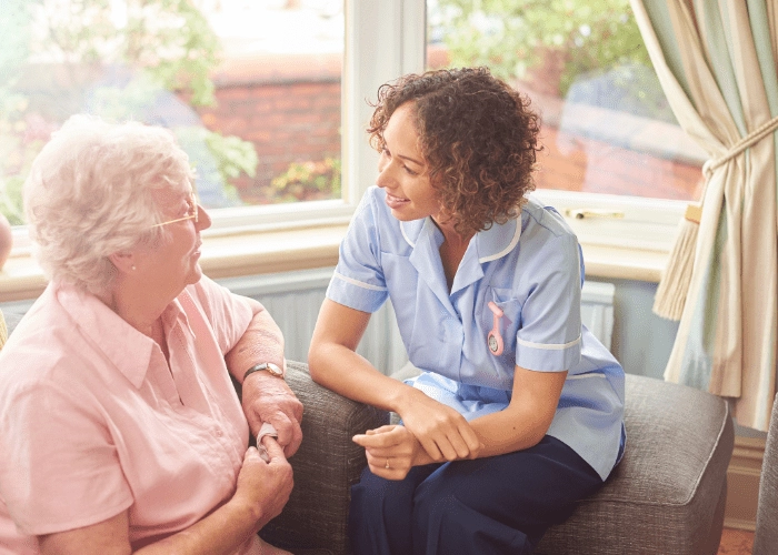Caregiver Certification - Home care nurse and elderly woman engaged in conversation in front of a sunny window. - MeetCaregivers