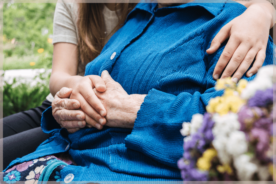 Caregiver training - Young woman hugging elderly woman while sitting in garden - MeetCaregivers