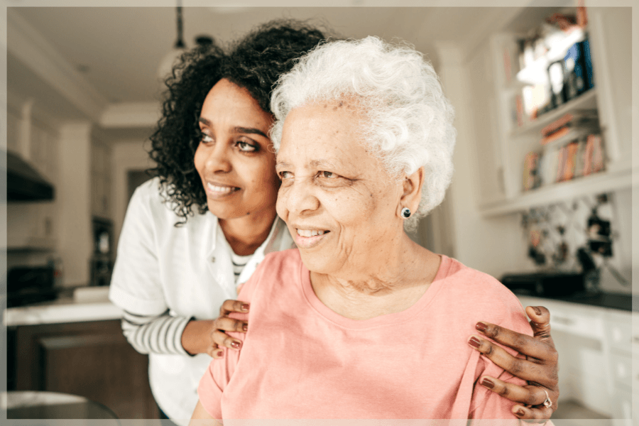 Professional caregiver hugging elderly woman in her kitchen - MeetCaregivers