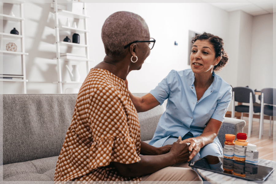 Professional caregiver talking to elderly woman about her medication at home - MeetCaregivers