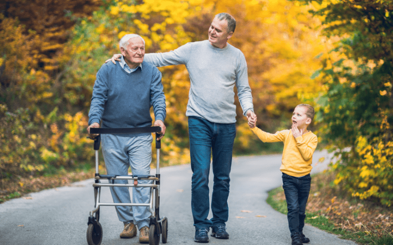 Man Walking In A Wooded Trail With His Elderly Father And Young Son