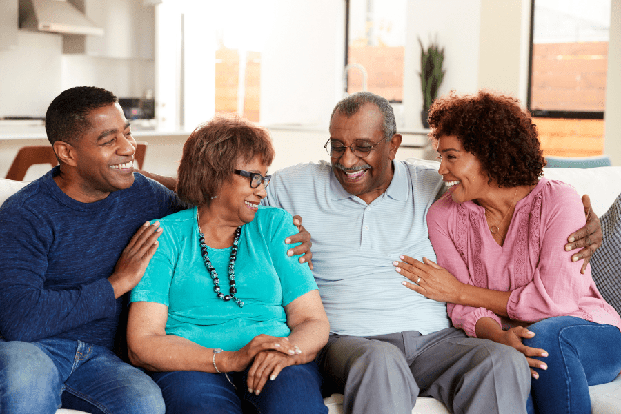 Happy older parents laughing on the living room couch with their adult son and daughter