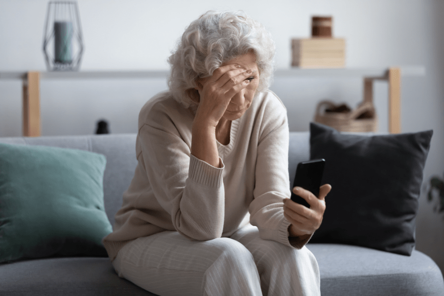 older-woman-with-compassion-fatigue-looking-at-her-phone-on-the-couch