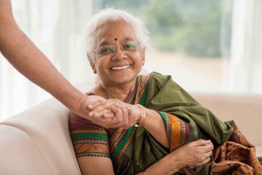 Smiling elderly woman dressed in traditional Hindi garb holding another persons hand