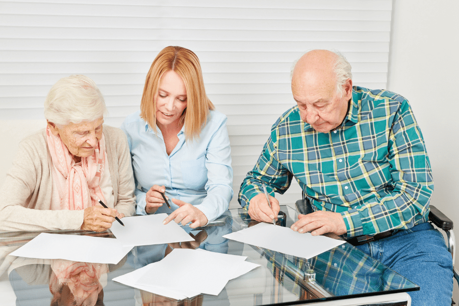 Lawyer explaining power of attorney vs. guardianship to elderly couple signing paperwork.