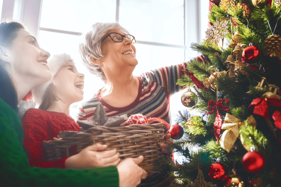 Mother, Daughter, & Granddaughter decorating a Christmas tree to ease holiday loneliness.