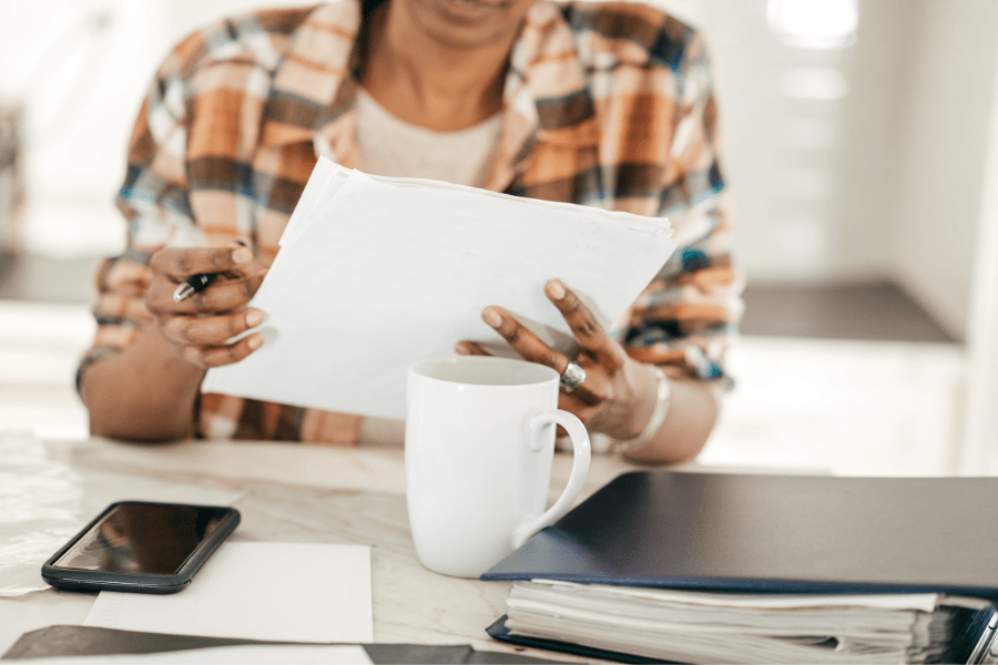 Woman with phone mug and binder reviewing paperwork.