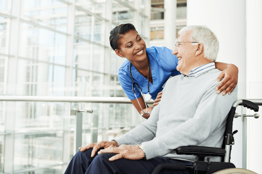 Certified Caregiver Chatting Happily With Elderly Man In A Wheelchair
