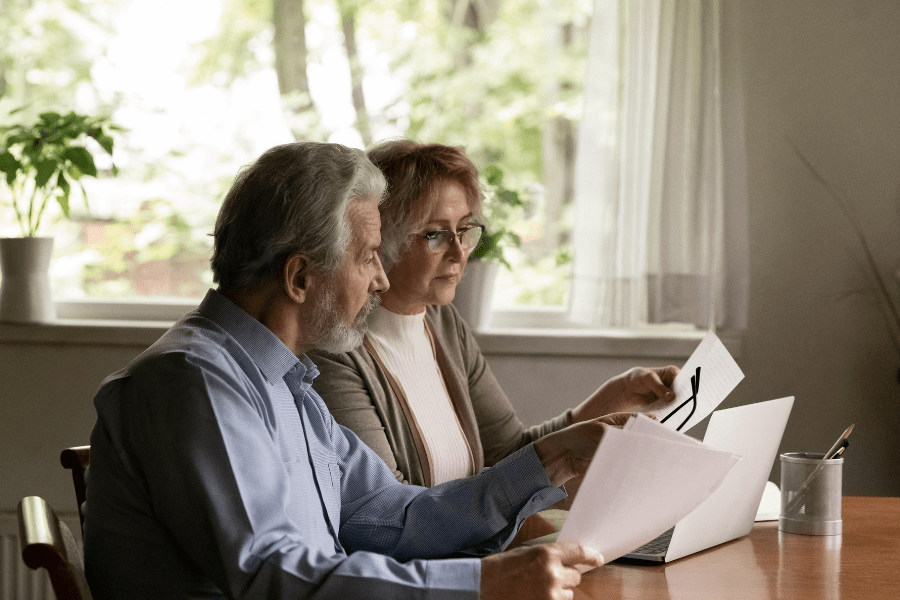 Medicare And Marketing Sales Summit – Older couple reviewing paperwork together at home.