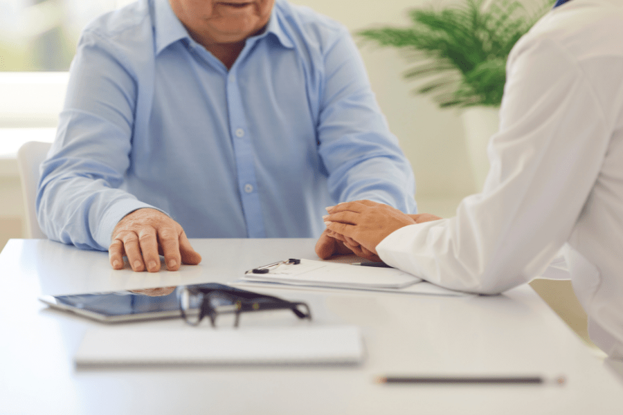 Doctor Touching Senior Mans Hands To Offer Comfort And Reassurance During Conversation In Hospital Room