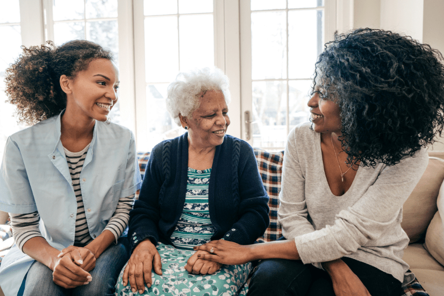 Elderly woman sitting on the couch with her adult daughter and caregiver.