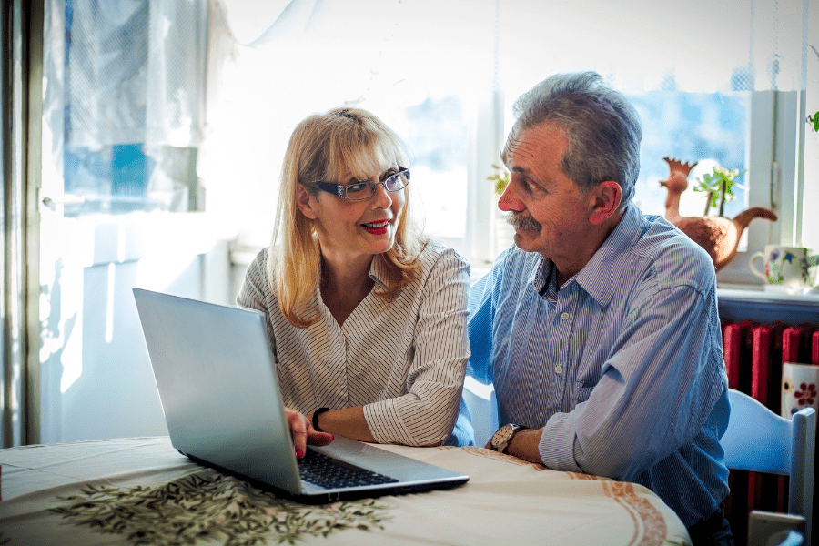 Older couple sitting at the table in front of a laptop researching a health plan.