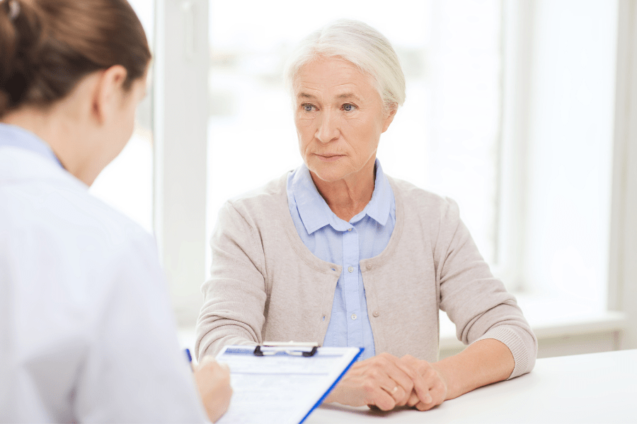 In-home care for elderly parents - Doctor taking notes on a clipboard while talking to senior woman