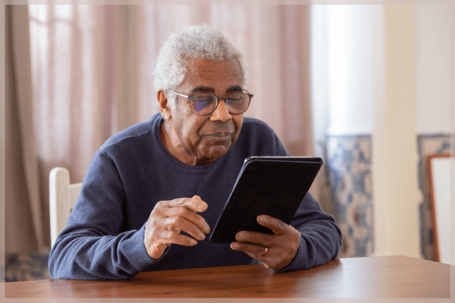 Save Your Vision Month - Senior man with glasses reading a tablet at the table - MeetCaregivers