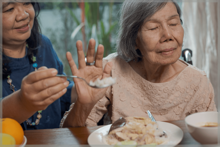 Senior nutrition Caregiver holding spoon of rice to elderly woman waving it away with her hand MeetCaregivers