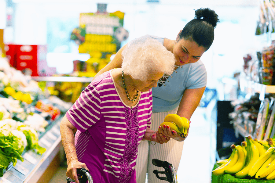 Dementia Home Care Worker And Elderly Woman Shopping For Produce At The Grocery Store