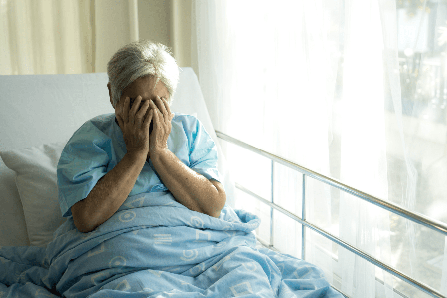 Lonely elderly patient sitting up in her hospital bed and covering her face.